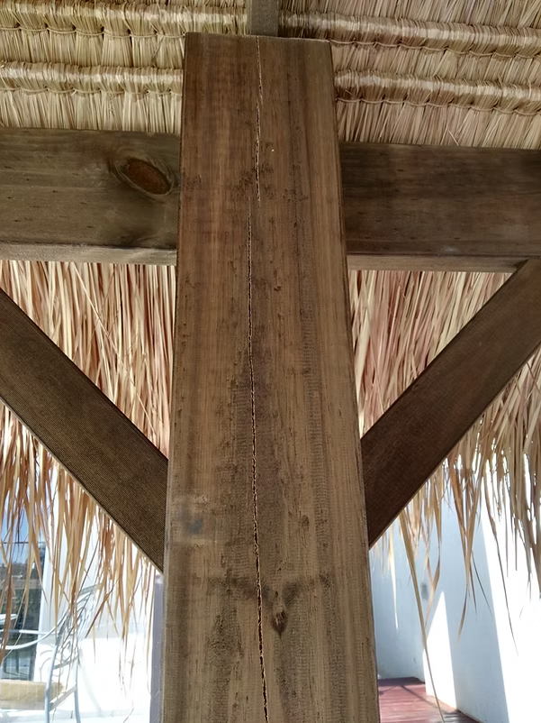 Vertical crack in a timber post beneath the thatched roof and braces
