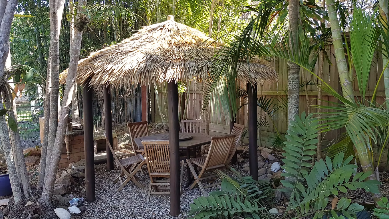 Synthetic thatch gazebo with a dining table in a tropical garden